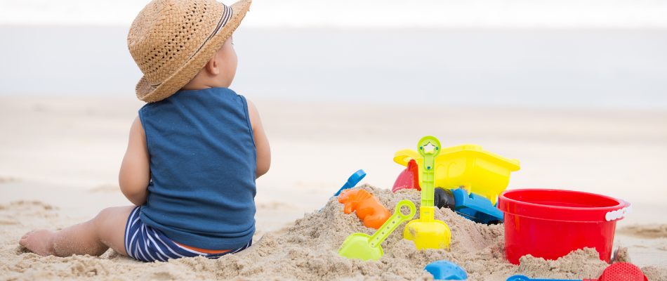 baby sitting on beach with hat and toys