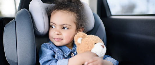 girl in car seat holding teddy