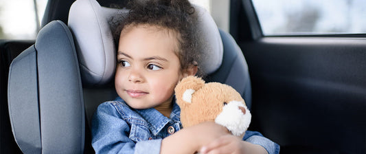 girl holding teddy in car seat in car